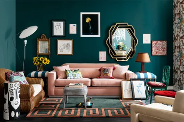 A maximalist living room with eclectic furniture, green walls, diverse art pieces, a pink sofa, and colorful cushions.
