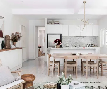 Modern kitchen with white cabinets, marble backsplash, stainless steel appliances, and wooden dining table with chairs.