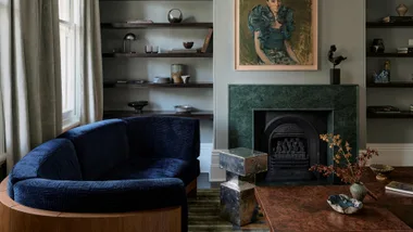 Luxurious living room with a deep blue curved sofa, green marble fireplace, modern art, and minimalist shelving.
