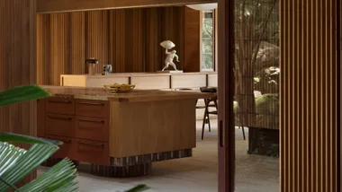 A modern wooden kitchen with an island, brown cabinets, and a statue resembling a figure holding a cloud.