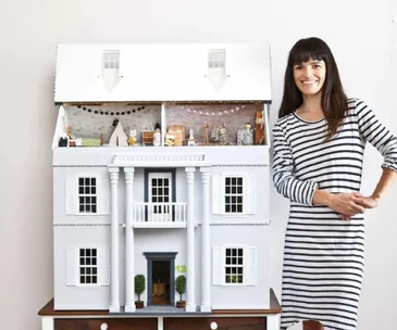 Woman wearing striped dress next to a large custom dollhouse
