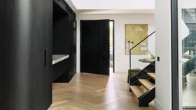 Engineered Timber Flooring laid in a herringbone pattern in the hallway of a modern home with black timber cabinetry and a black timber clad front door leading out to the street.
