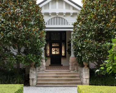 traditional home with stone front steps surrounded by large shade trees