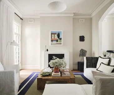 Luxurious living room with a white sofa, coffee table with flowers, abstract art, and modern decor.