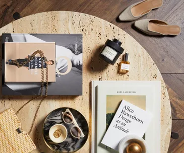 Books, perfume, and sunglasses arranged on a round table with a pair of shoes nearby.