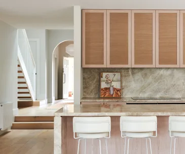 Kitchen with quartzite stone and timber-veneer joinery with view of arched hallway and stairs in renovated period home