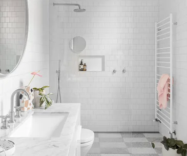 Modern white bathroom with a shower, vanity, plants, and a towel on a heated rack.
