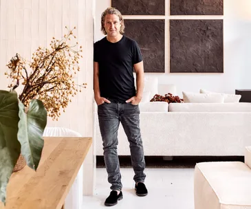 Founder Charlie Hinckfuss stands in the MCM House Paddington showroom wearing a black t shirt and jeans surrounded by neutral coloured furniture.