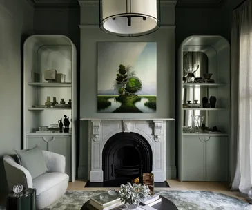 Sophisticated living room with a marble fireplace, artwork, built-in shelves, and soft green-gray walls.
