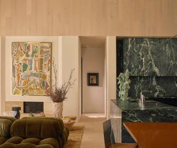 Luxurious interior with abstract art, green marble kitchen island, plush seating, and decorative plants.