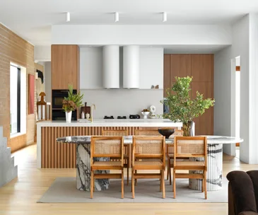 A neutral-toned open-plan living area with a marble dining table and timber-clad island bench