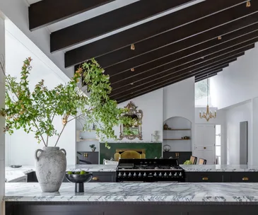 A modern kitchen with marble countertops, parquetry flooring and exposed timber beams