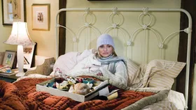 Woman lying in bed with purple beaning, red bed cover and a tray of food, from the movie The Holiday.