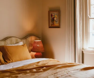 A cosy bedroom styled with orange bedding and a rattan bedside lamp