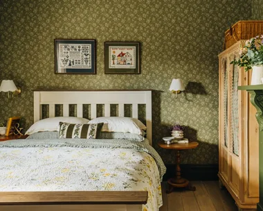 A country bedroom with green floral wallpaper and frilly country-style bedding