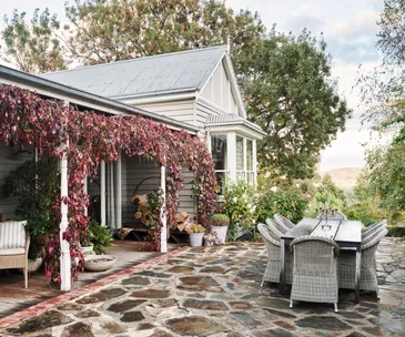 An alfresco area overlooking rolling hills beside a cottage with a vine covered verandah