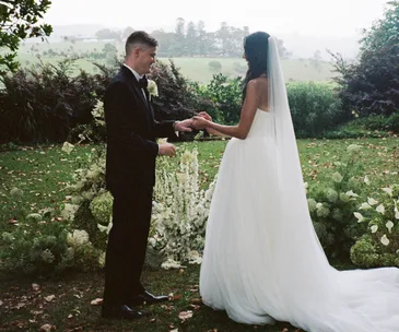 A couple exchange wedding rings in a field