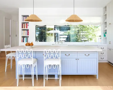 A bright country-inspired kitchen with a blue island bench and two rattan pendants