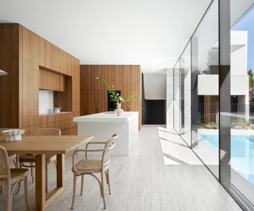 An open-plan kitchen and dining area with floor-to-ceiling windows looking out to a swimming pool