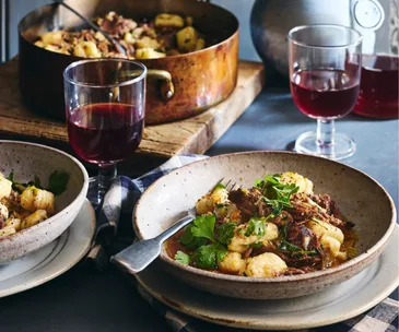 A bowl of slow-braised lamb gnocchi with anchoiade and glasses of red wine