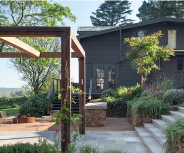 A dark grey weatherboard home beside a pergola and garden beds