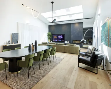 A dining room with a large black dining table, green velvet chairs and black accents.