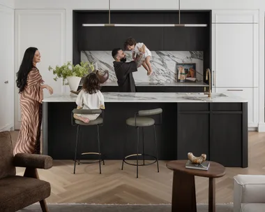 Matty and Sarah Fahd with their two children in their renovated kitchen with stone benchtops and a hanging pendant light